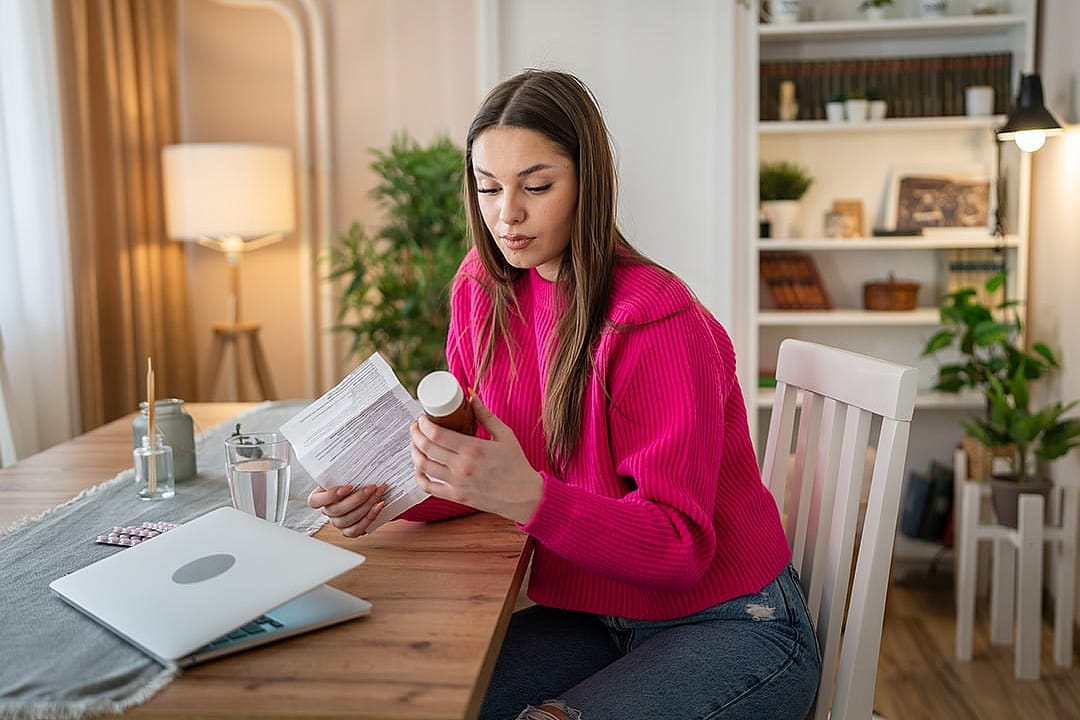 A young woman at home reading hospital bills and prescriptions.